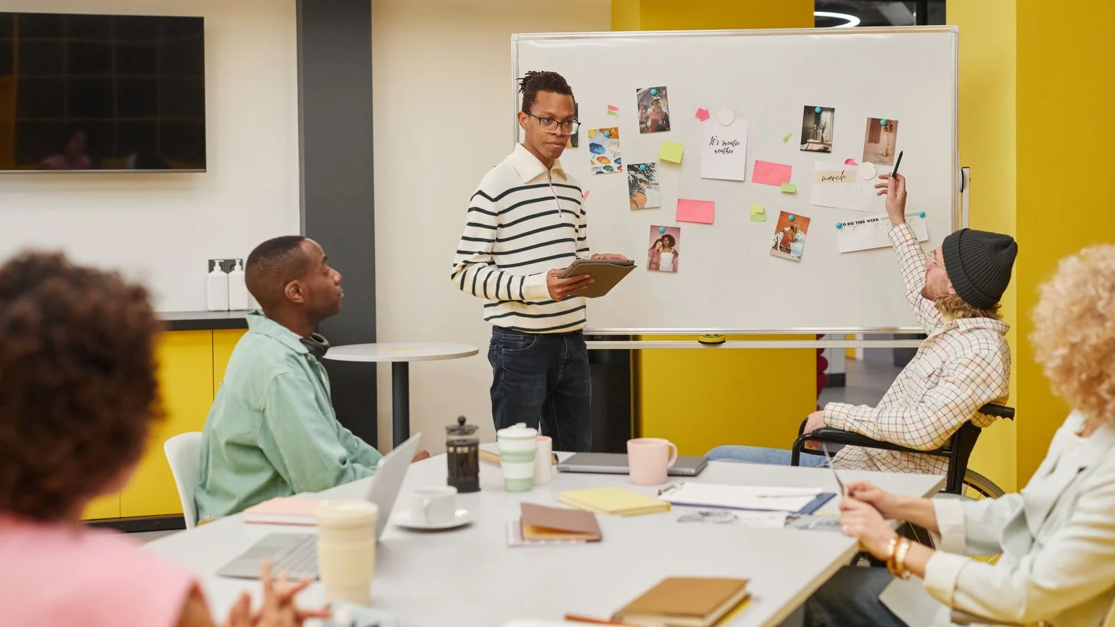 A facilitator and diverse adult colleagues discussing ideas at a whiteboard during an office workshop