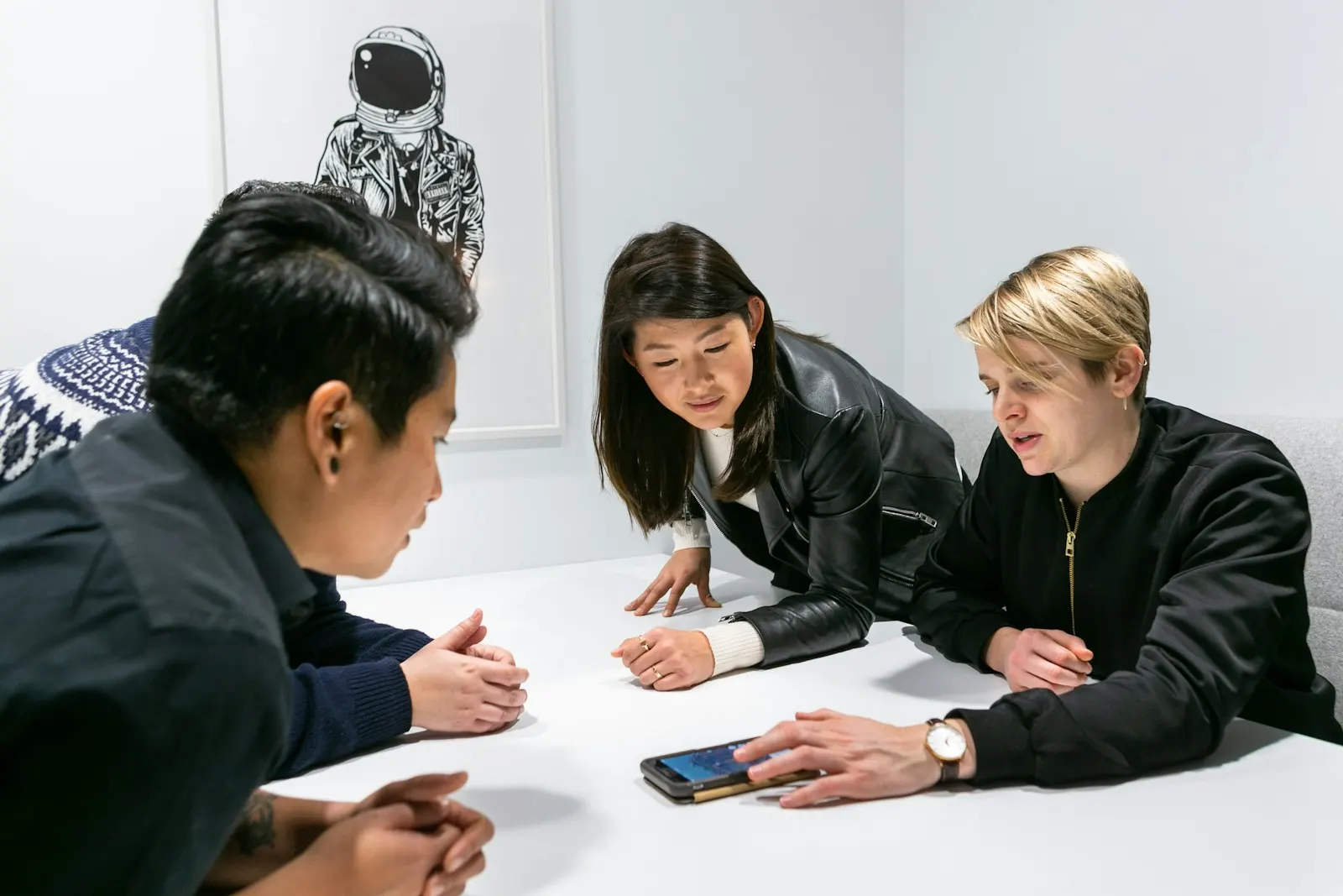 Colleagues leaning in around a meeting table to share perspectives while one explains an idea on a phone