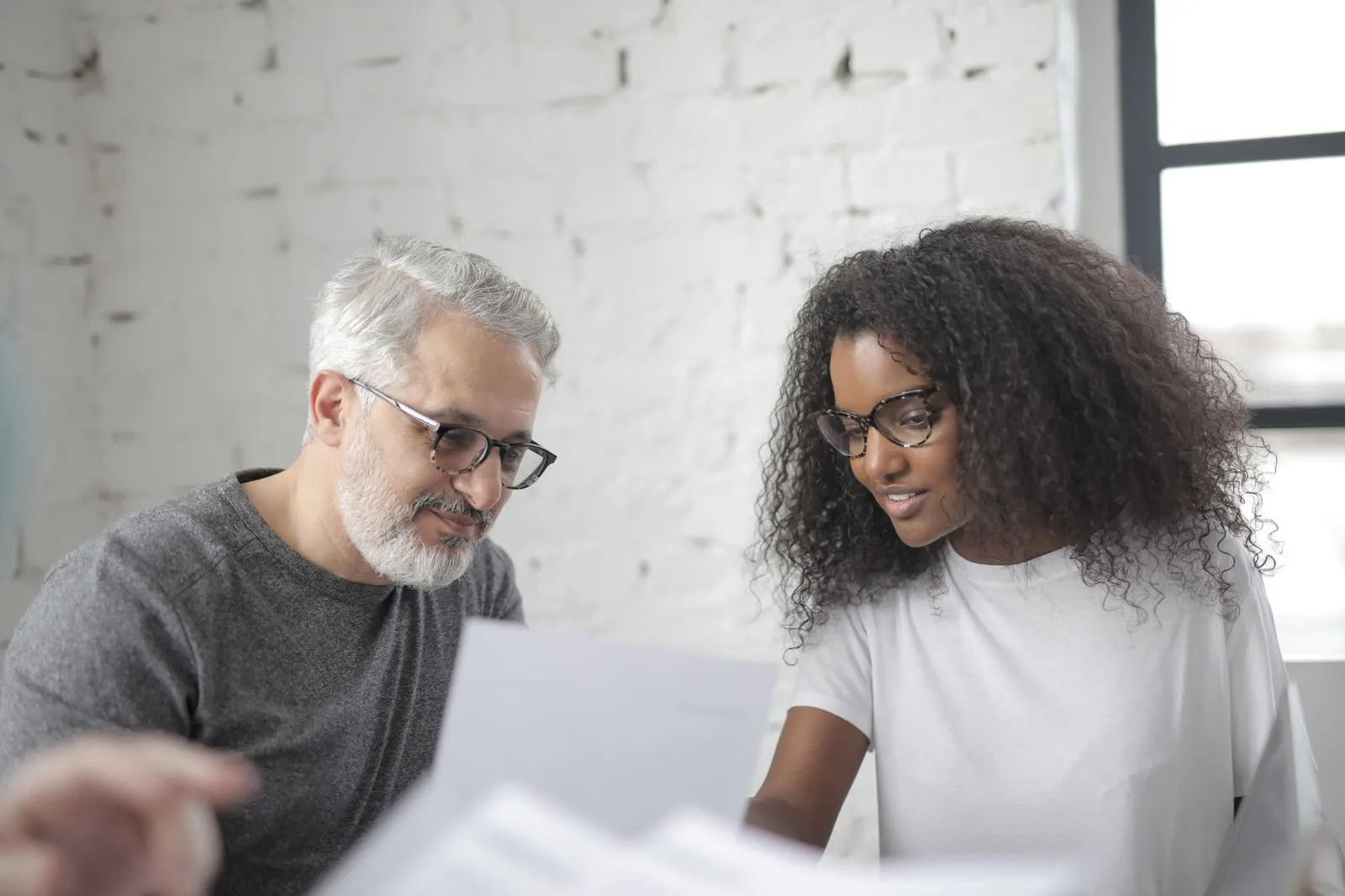 An experienced mentor and a younger colleague reviewing a document together at a shared desk